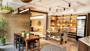 Un interior moderno con una mesa de comedor de madera, sillas y un suelo estampado. Hay estanterías con diversos objetos y un refrigerador.