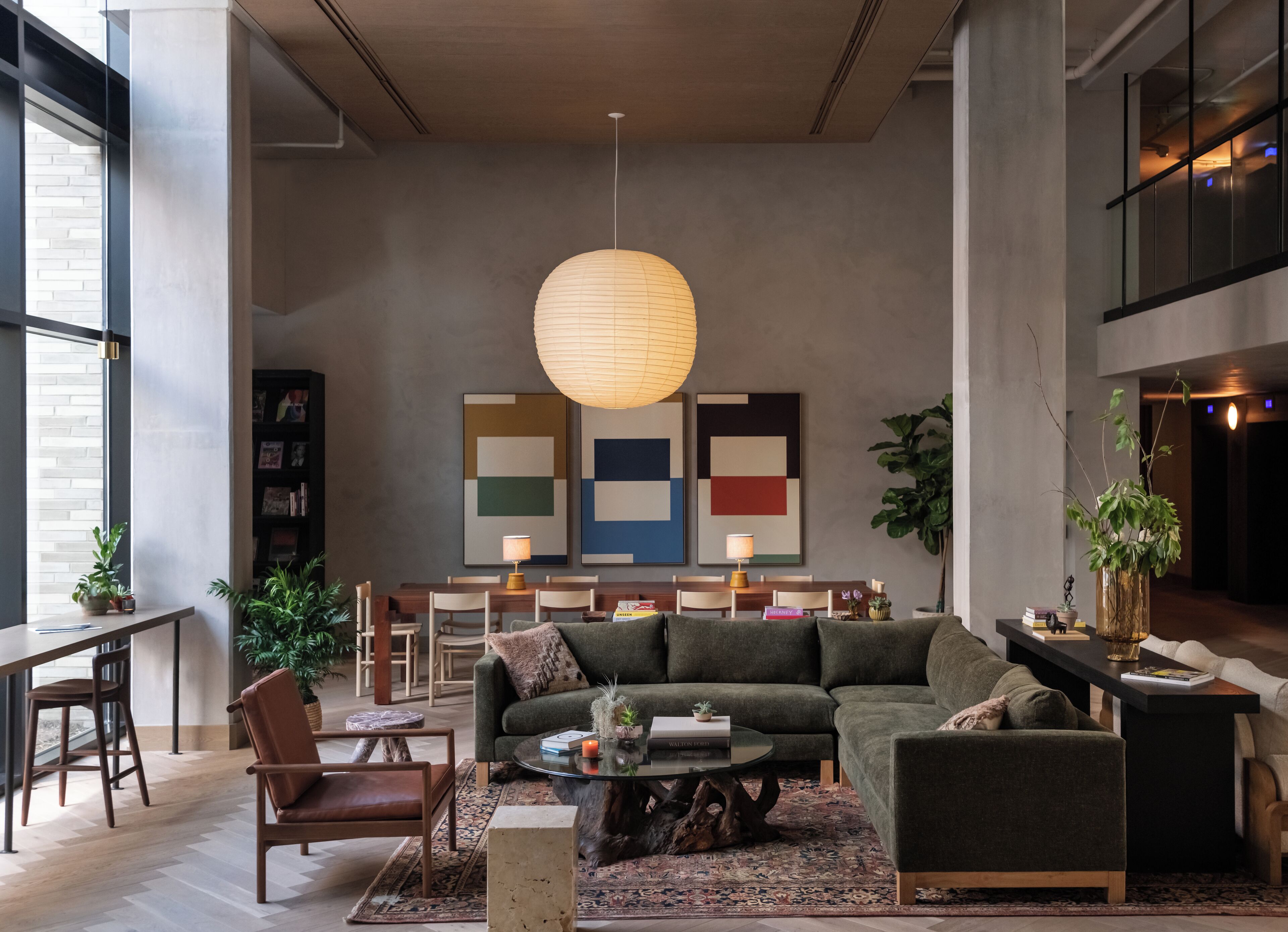 Een moderne woonkamer met een modulaire bank, een salontafel en een eethoek met stoelen en een tafel. Op de muur hangen abstracte schilderijen en er is een grote hanglamp.