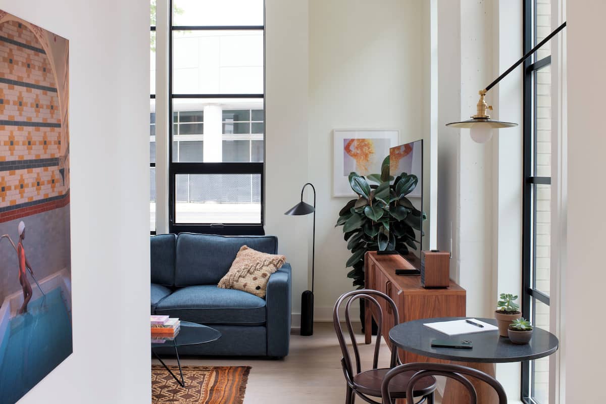 A modern living room with a blue sofa, a coffee table, a small dining table, and a large plant.