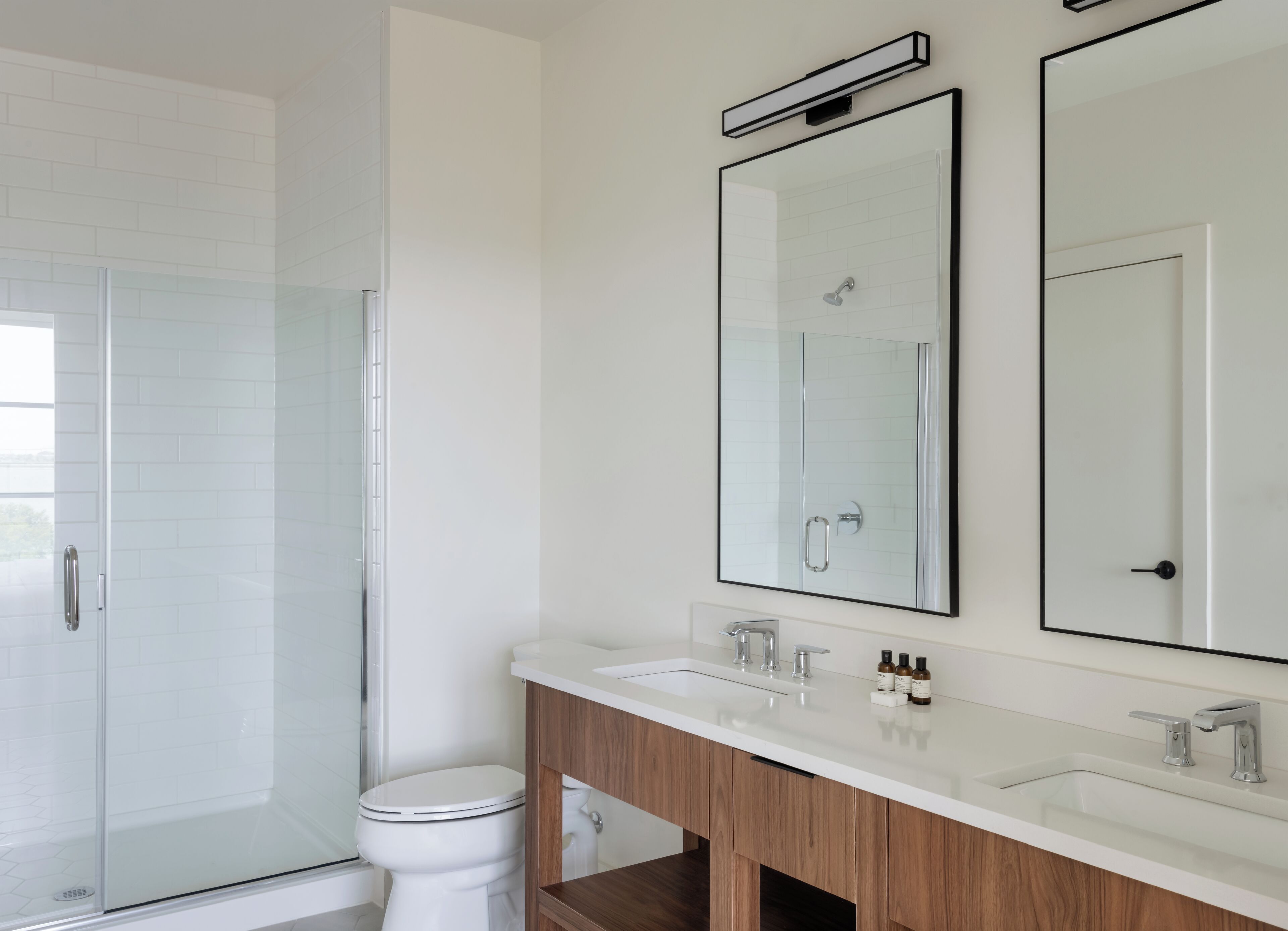 A modern bathroom with a glass shower enclosure, a toilet, a vanity with a mirror, and a sink.
