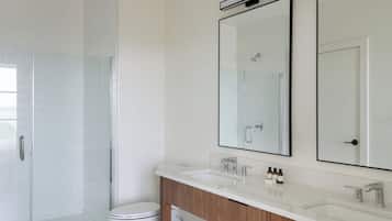 A modern bathroom with a glass shower enclosure, a toilet, a vanity with a mirror, and a sink.