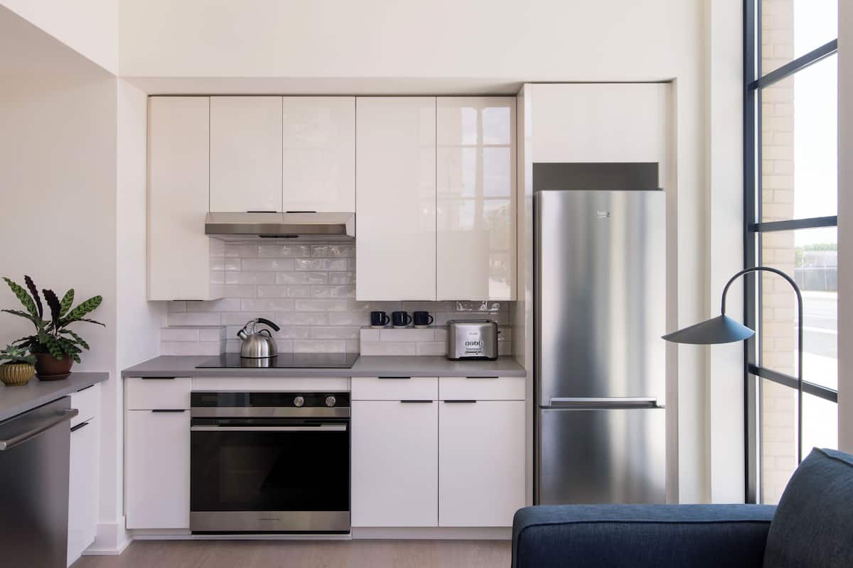 A modern kitchen with white cabinets, a stainless steel refrigerator, a built-in oven, and a kettle on the countertop.
