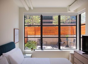 A bedroom with a large window, a bed, a bedside table, a lamp, and a TV.