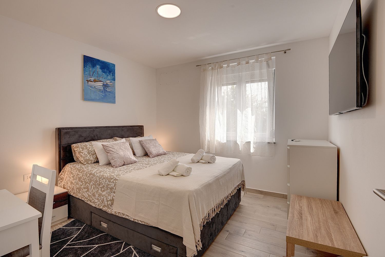 Una camera da letto con un letto, una scrivania, una sedia, una TV e un quadro appeso al muro.