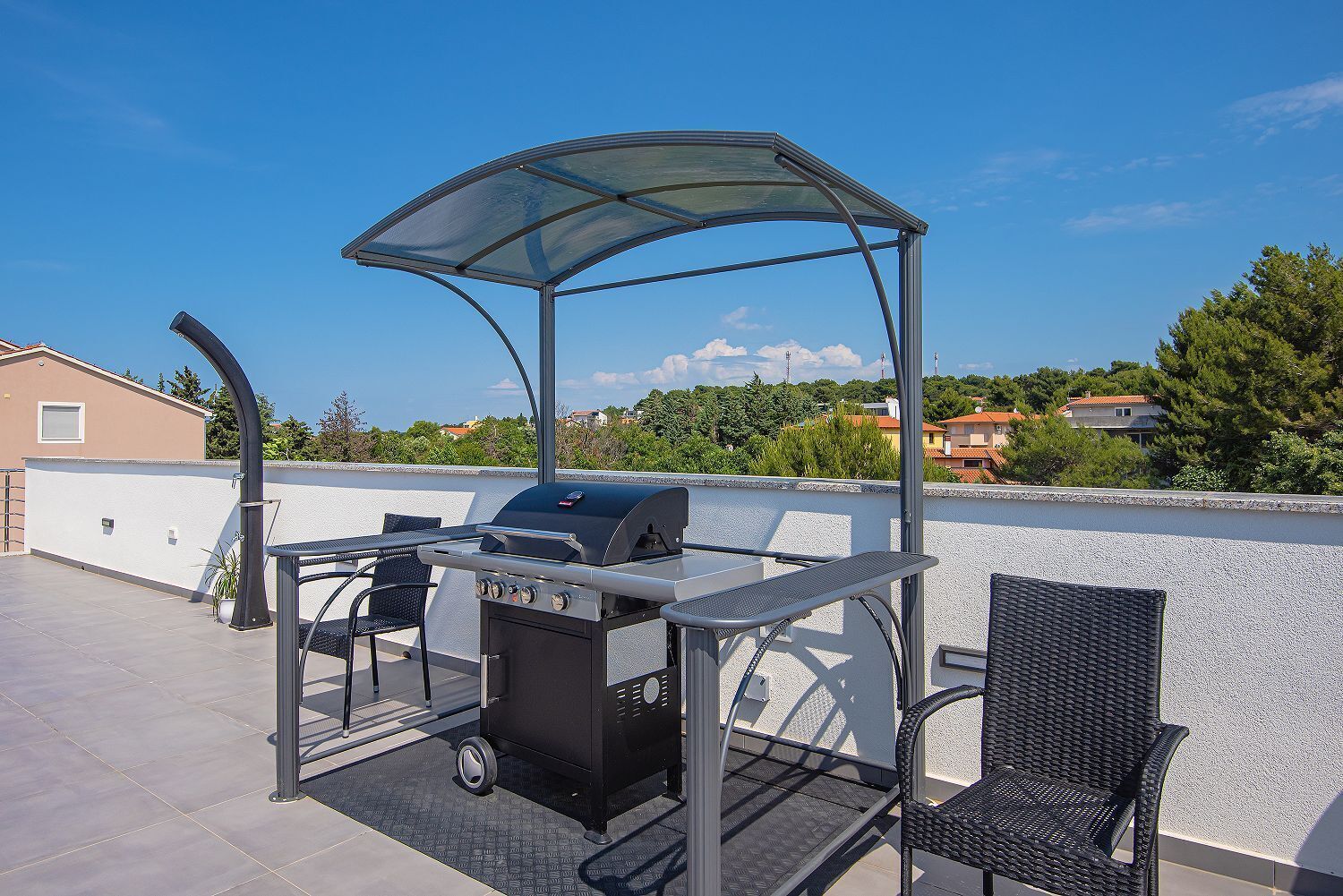 Een terras buiten met een barbecue, stoelen en een overdekte zithoek.