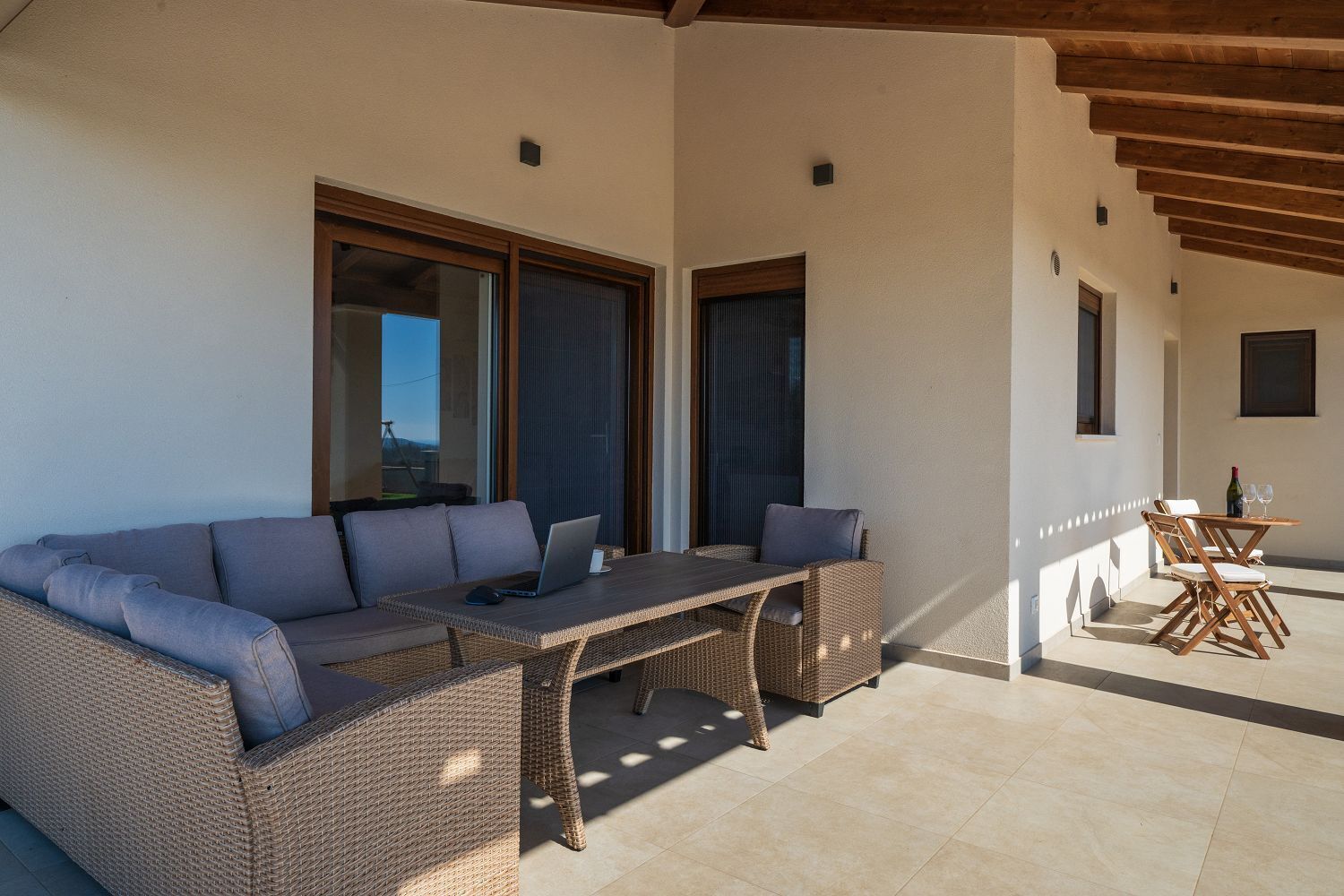 Un'area salotto esterna coperta con un divano in vimini e un tavolino, un balcone con vista e un tavolo in legno con sedie.