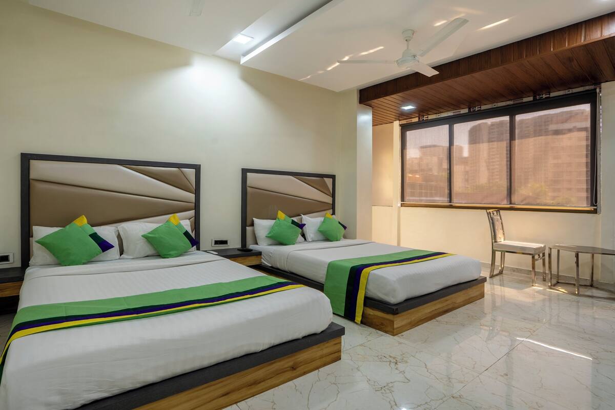 A hotel room with two beds, a ceiling fan, a window with a view, and a chair.