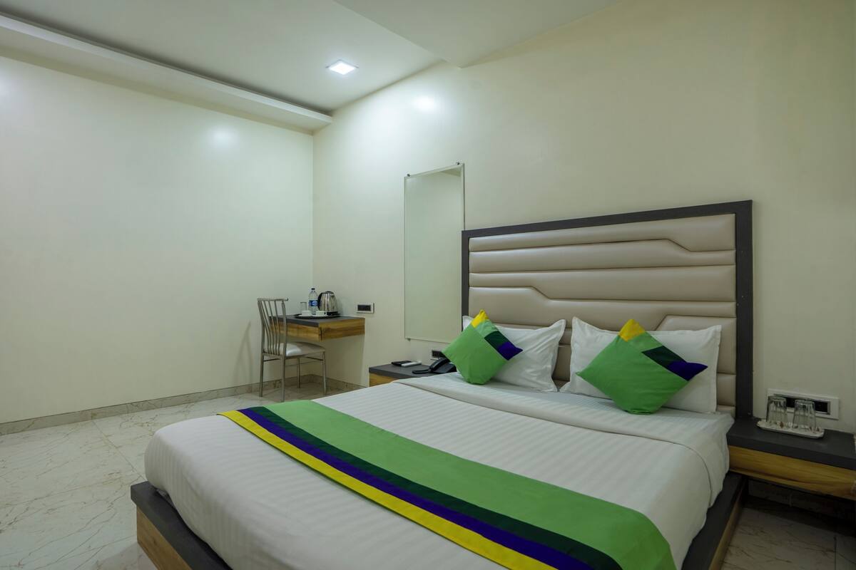 A hotel room with a bed, a desk, a chair, a nightstand, and a mirror.