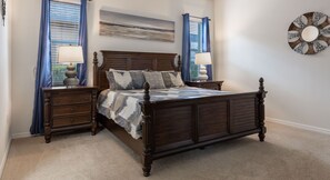 Un dormitorio con una cama de madera con dosel, dos mesitas de noche, un ventanal con cortinas azules, un reloj en la pared y un cuadro de paisaje.