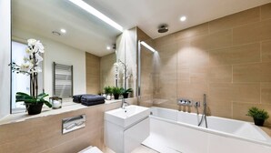 Un baño moderno con bañera, lavamanos e inodoro. Hay plantas en macetas y un espejo en la pared.