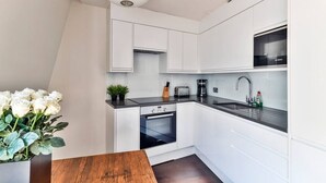Una cocina moderna con gabinetes blancos, encimera negra, horno integrado, un lavamanos y una cafetera.