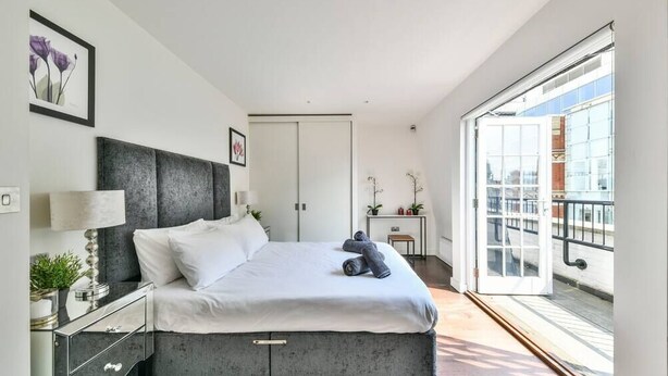 Un dormitorio moderno con una cama, mesita de noche y vistas al exterior.