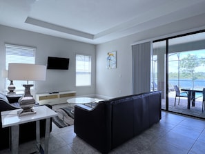 Relax in a stylish living room with a sleek sofa, flat-screen TV, and sliding glass door leading to a serene outdoor space.