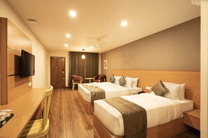 Een hotelkamer met twee bedden, een bureau, stoelen, een televisie en een plafondventilator.