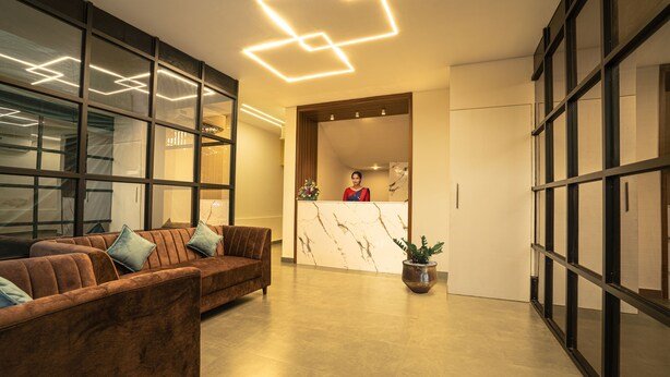 A modern lobby with a reception desk, a brown sofa with cushions, and a potted plant. - ADDRESS7 Hotel Kalamassery (Kanayannur)