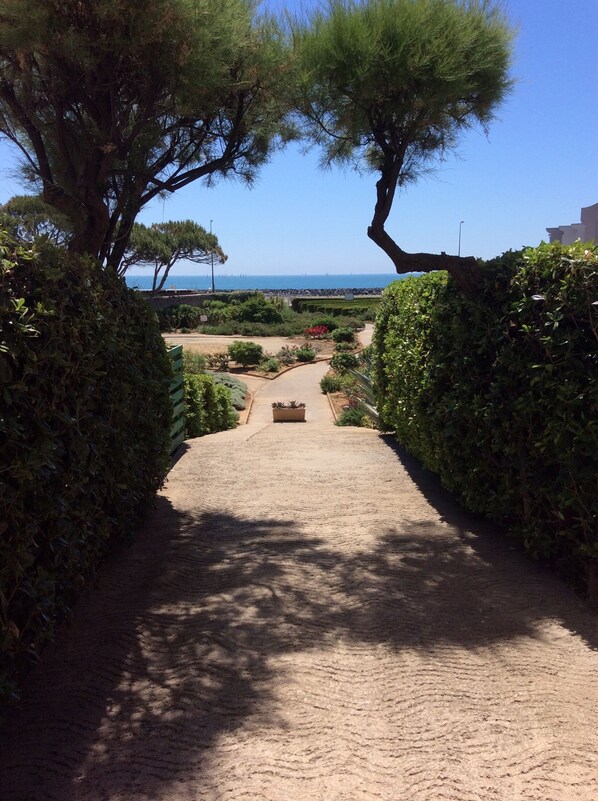 A paved pathway leading to a beach with a clear view of the sea.