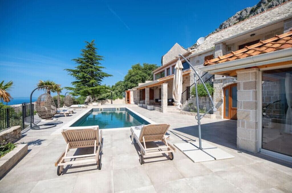 A poolside area with lounge chairs, a clear blue sky, and a view of the sea.