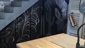 A staircase with a stone wall on one side and a black wall with a cactus and leaf pattern on the other. There is a wooden table with a black faucet in front. - Maison de Village Située Dans un Hameau Très Calme , Agréable à Vivre (saint julien du serre)