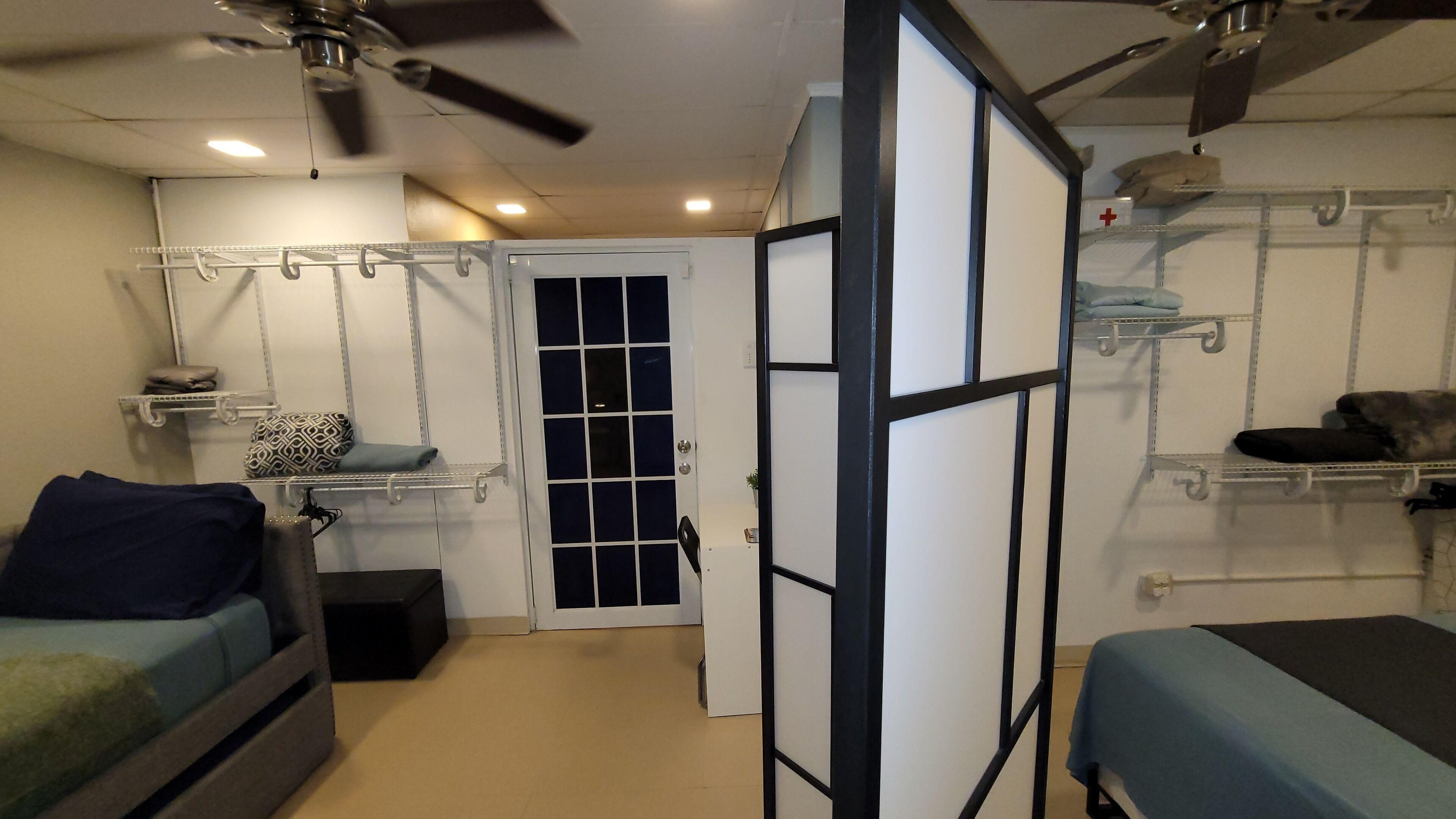 A compact bedroom with a bed, a small seating area, and a wardrobe with shelves.