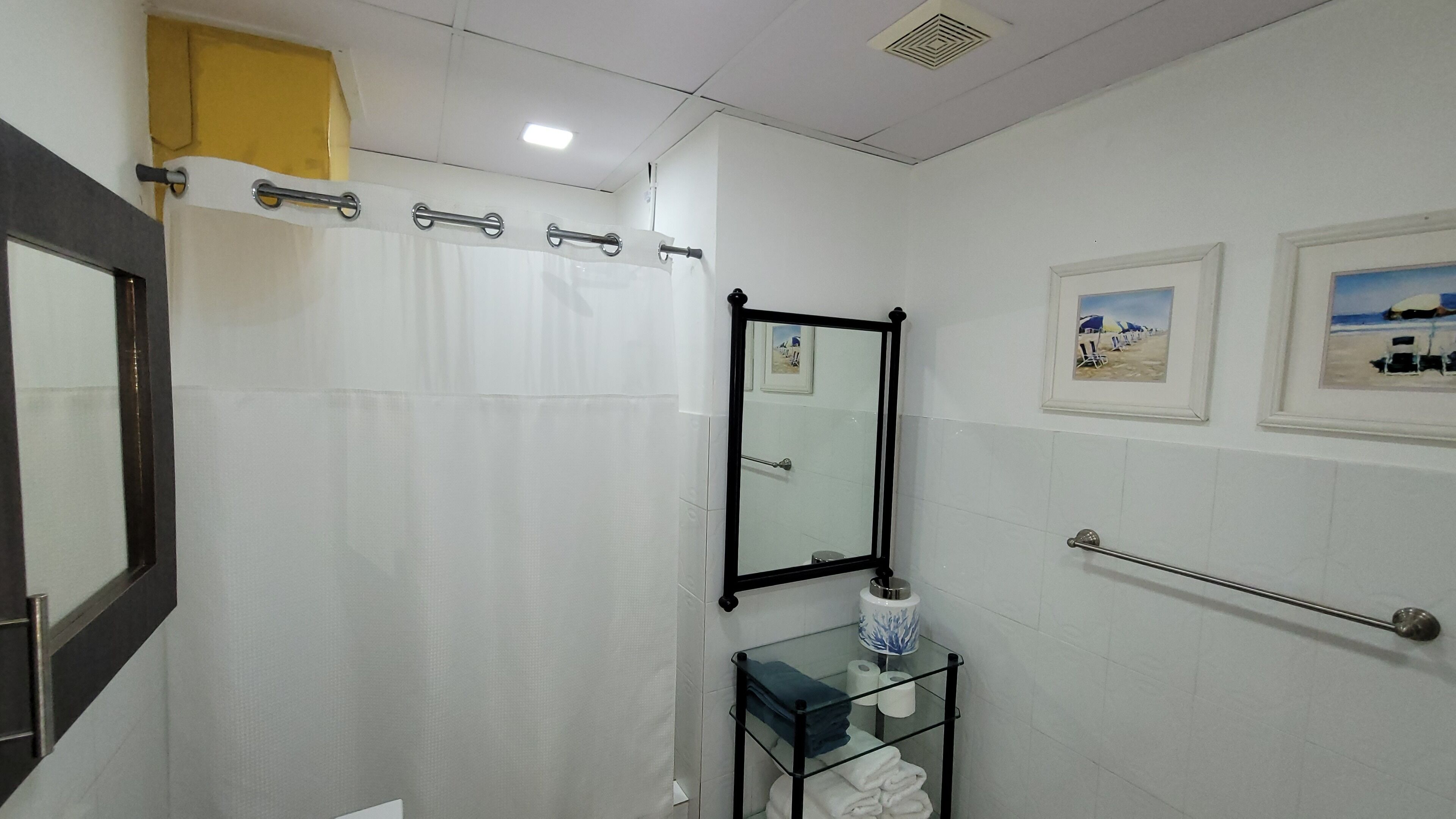 A bathroom with a glass shelf holding towels, a shower curtain, and a mirror on the wall.
