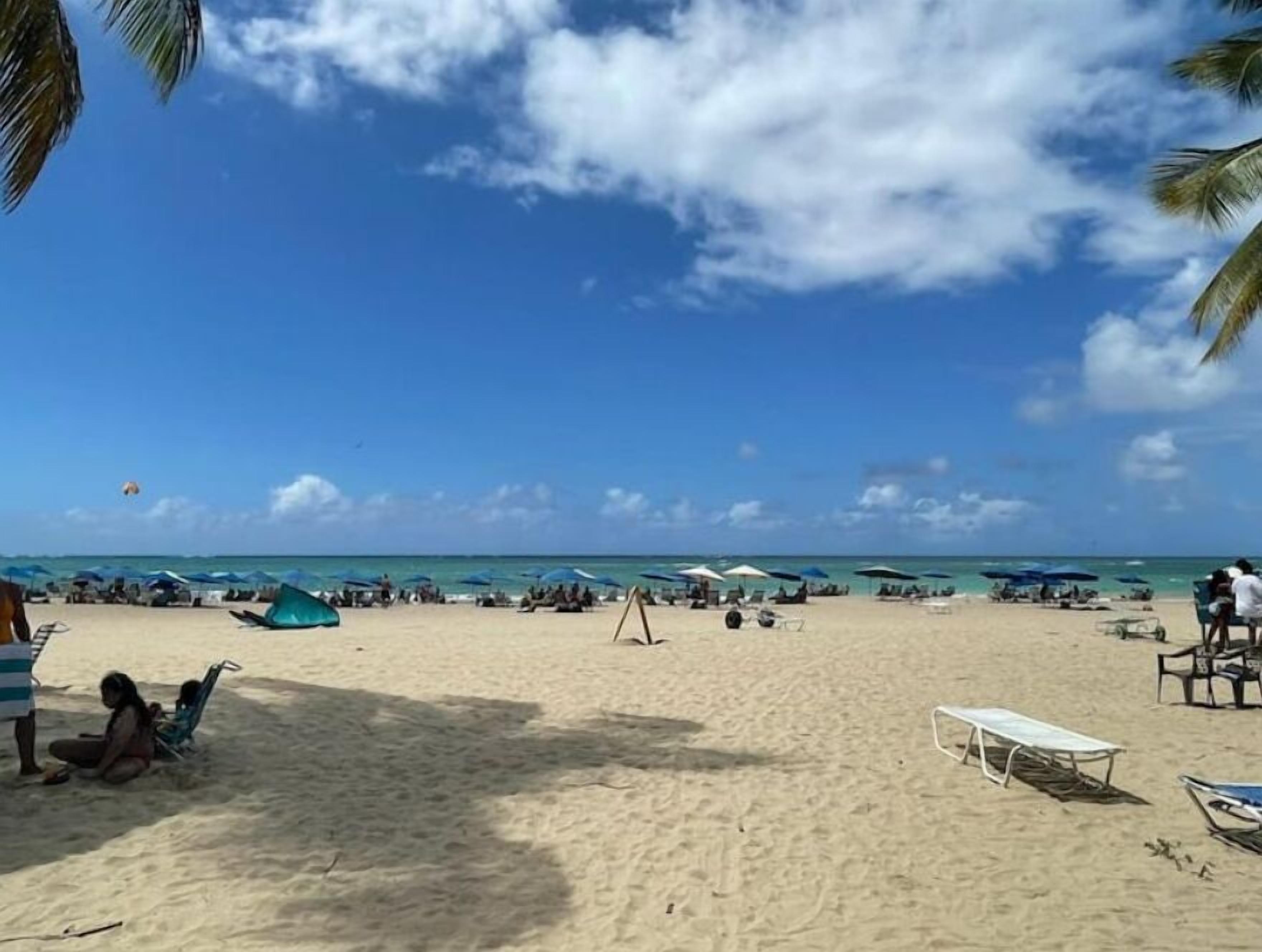 A beach with umbrellas, lounge chairs, and a clear sky.