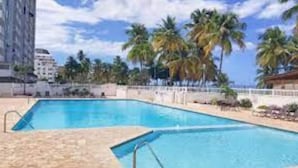 Une piscine à l’eau d’un bleu cristallin, entourée de palmiers et délimitée par une clôture blanche.