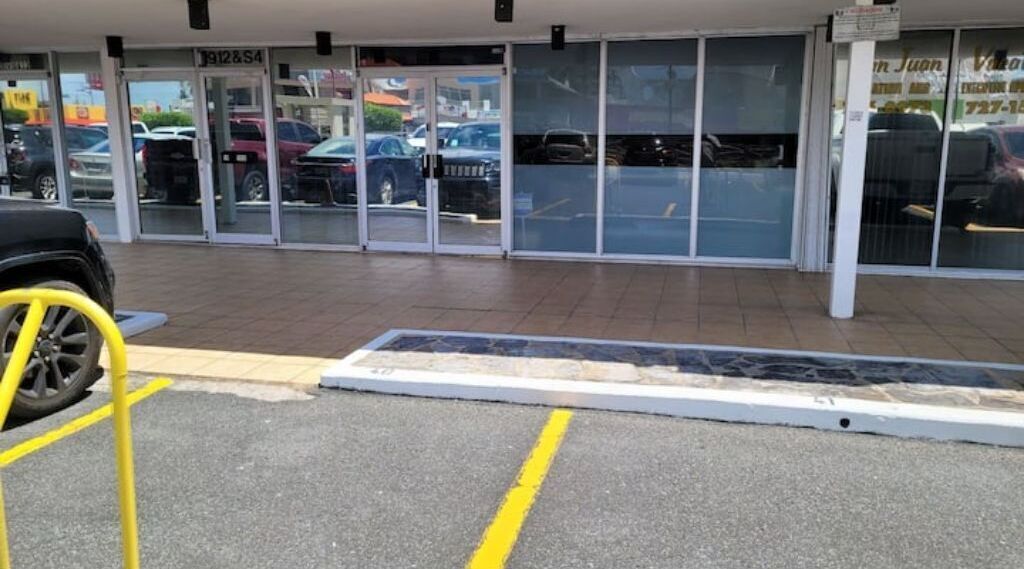 A parking lot with a yellow barrier and a building entrance with glass doors.
