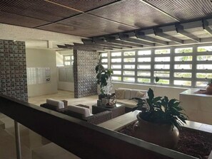 Een modern interieur met een zithoek, een potplant en uitzicht door een raam met een rasterpatroon.