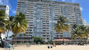 Un grand hôtel avec de nombreux balcons, situé près d’une plage bordée de palmiers.