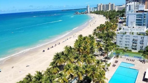Un hôtel situé en bord de mer, doté d’une piscine, de palmiers et offrant une vue sur l’océan.