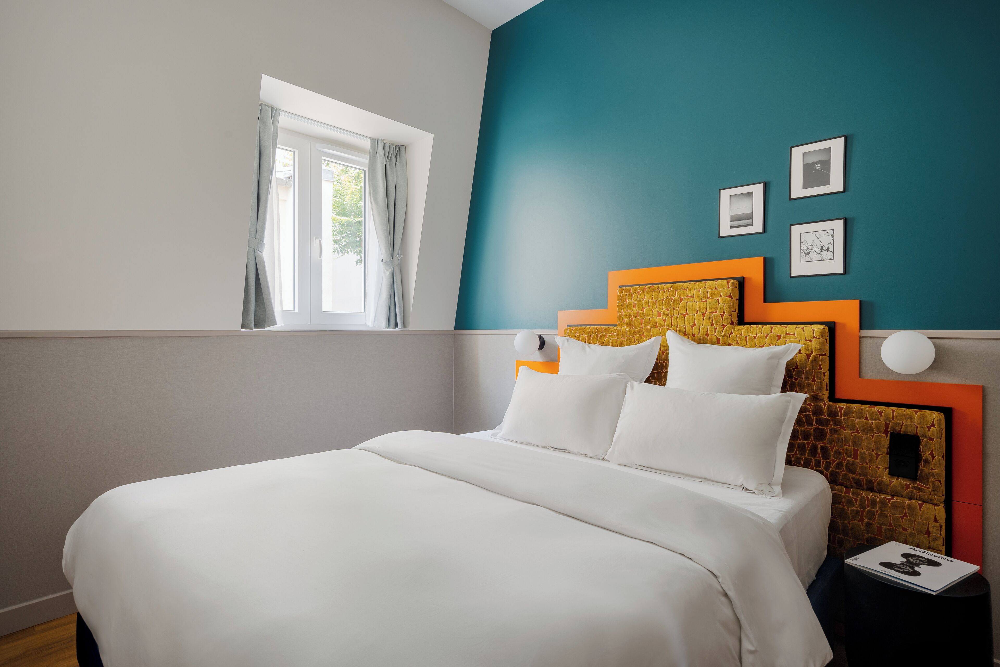 Une chambre à coucher avec un lit, une fenêtre avec des rideaux et un mur orné de tableaux.