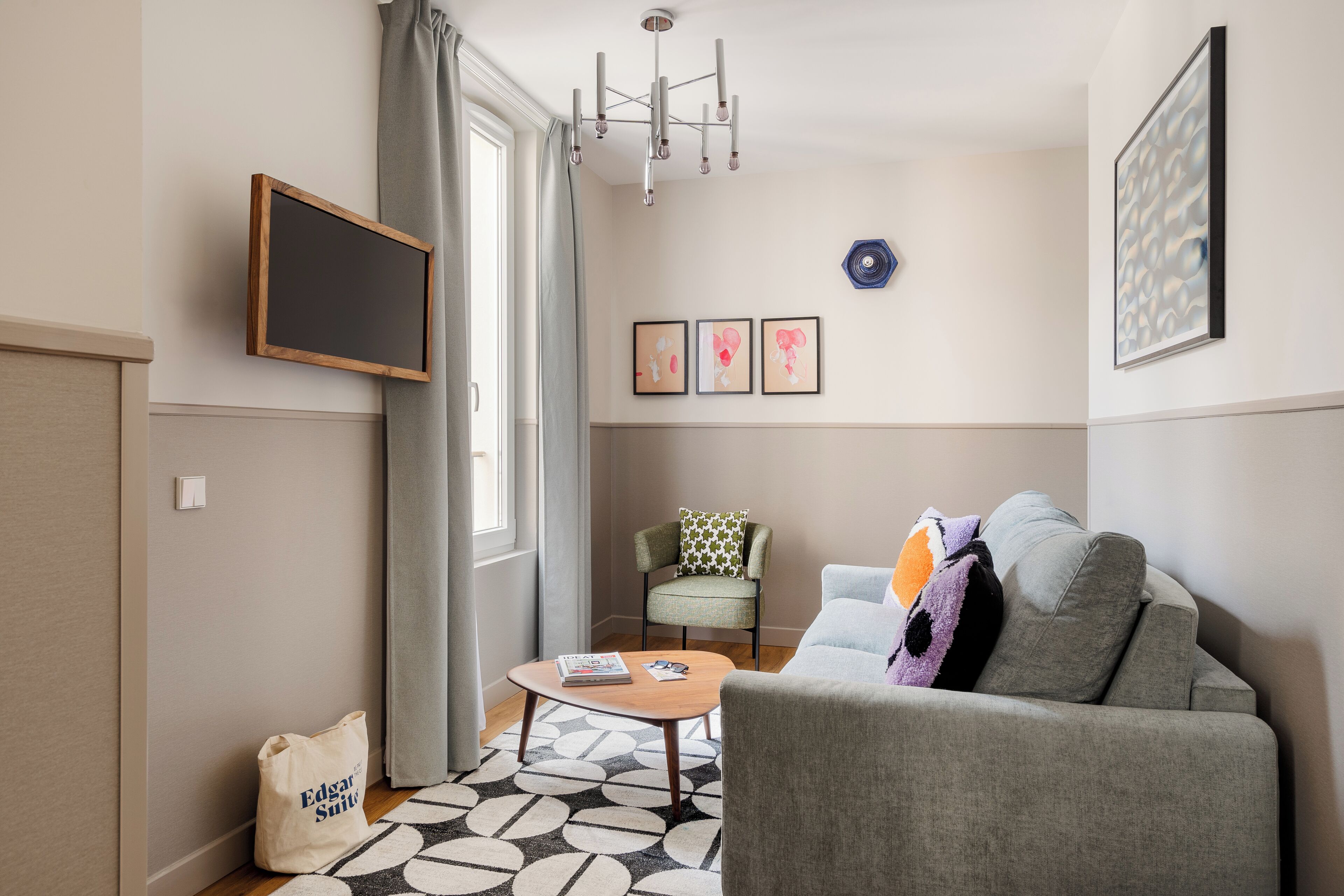 A modern living room with a grey sofa, a small round table, a green armchair, and a large window with curtains.