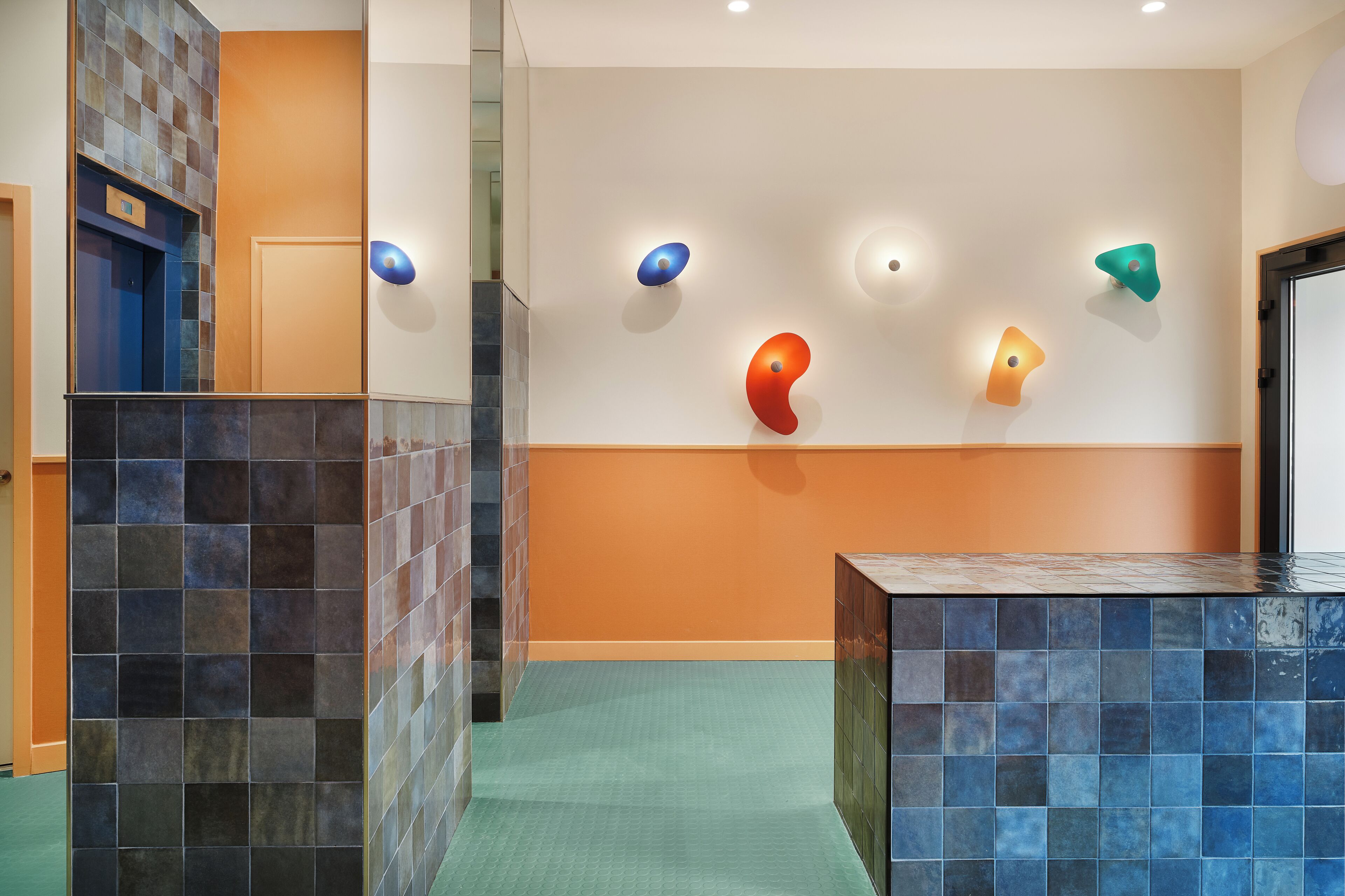 Un hall d’entrée avec un sol carrelé, un comptoir d’accueil et un mur orné d’œuvres d’art abstraites.