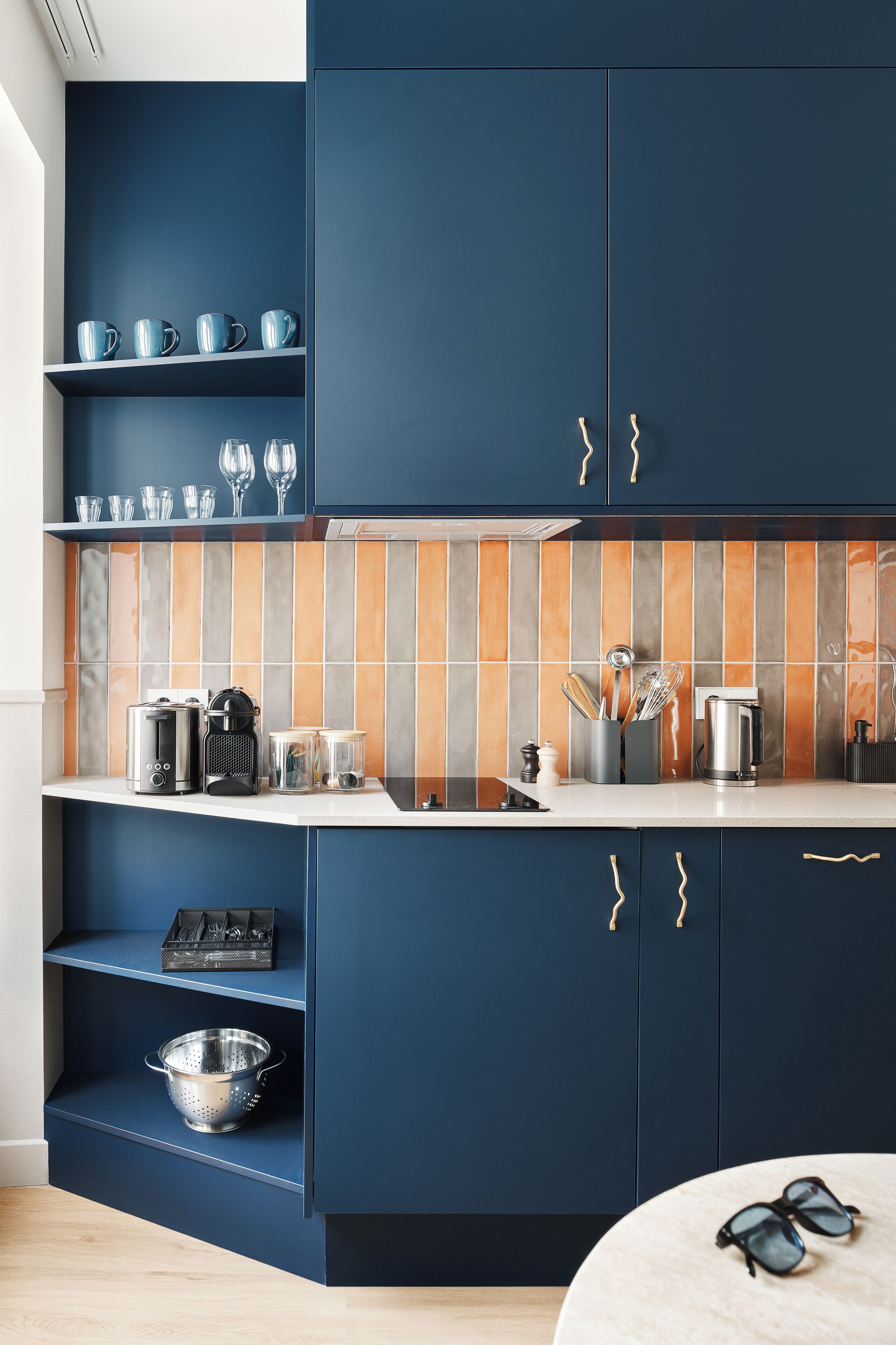Cozinha moderna com armários azul escuro, bancada branca e painel de azulejos.