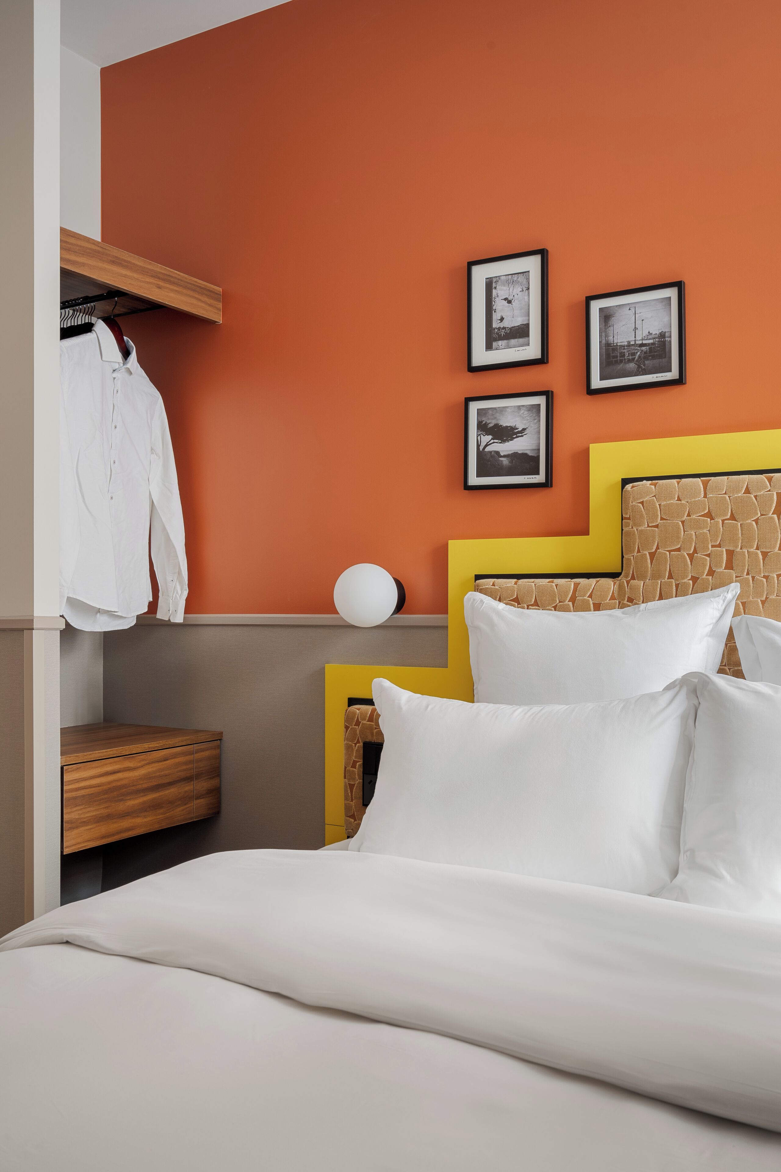 A neatly made bed with white linens, a wooden nightstand with a lamp, and a wall with framed pictures.