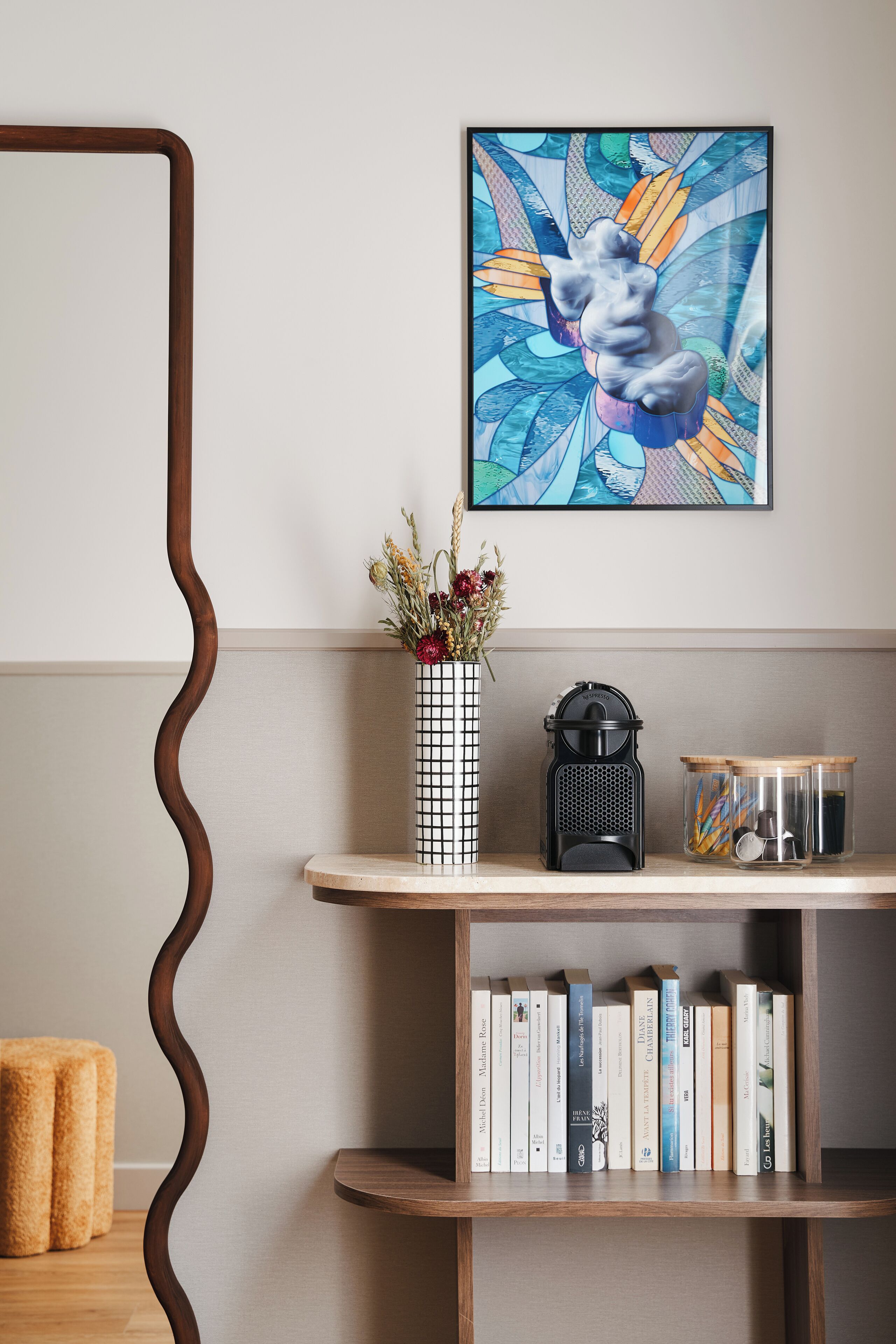 Ein Bücherregal mit Büchern, eine Vase mit Blumen und ein gerahmtes Kunstwerk an der Wand.
