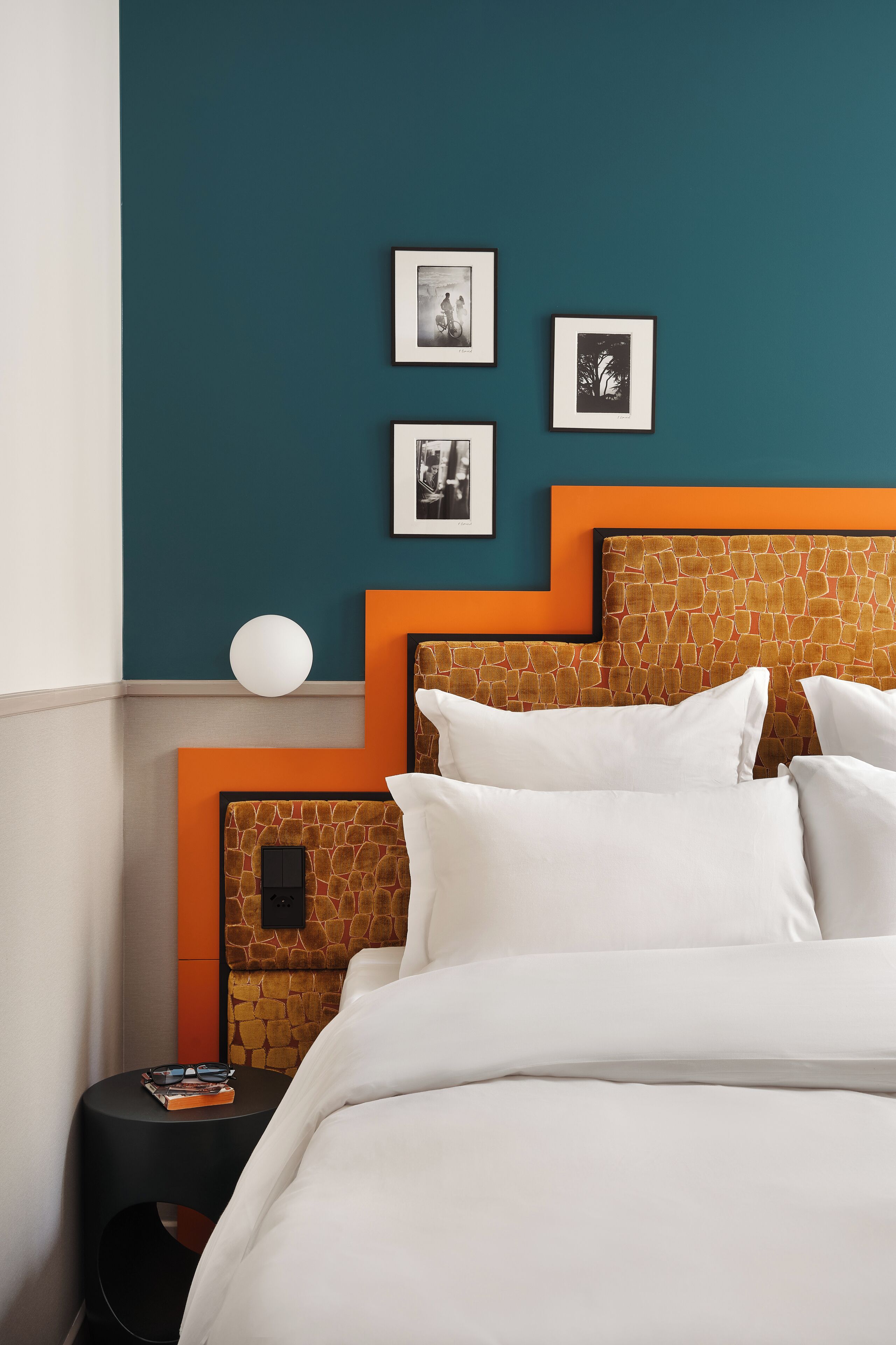 A neatly made bed with white linens, a headboard with a stone pattern, and a wall with teal and orange accents.