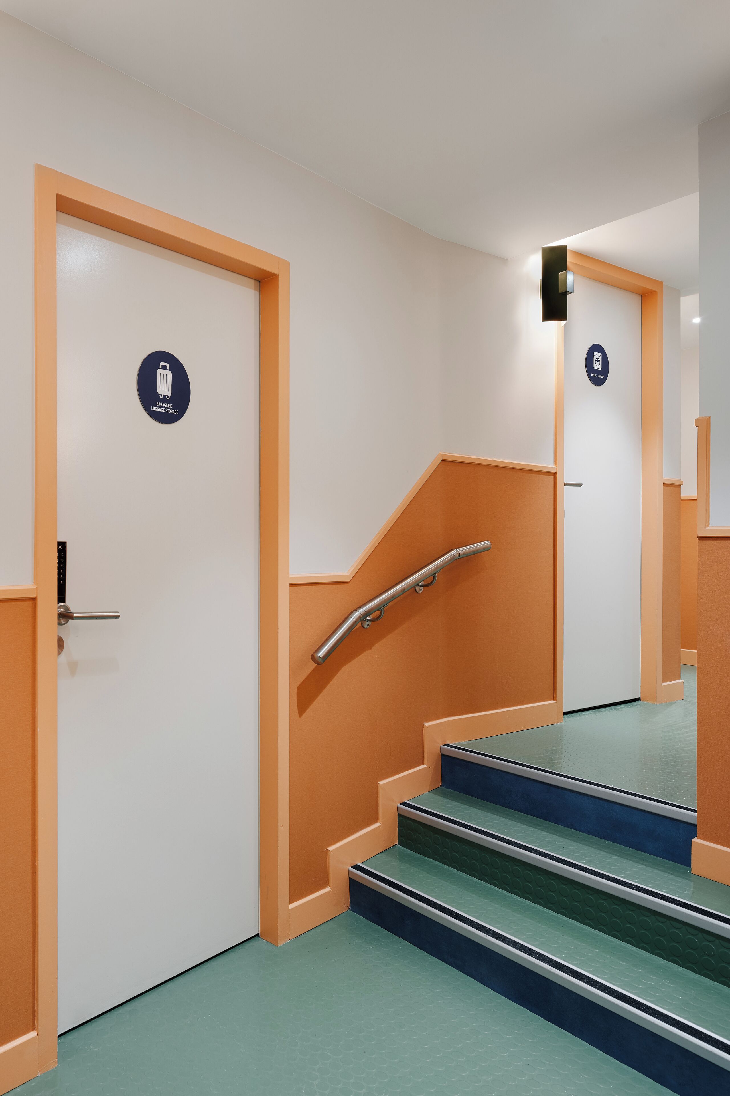 Un escalier avec des rampes, une porte avec une pancarte et un luminaire fixé au mur.