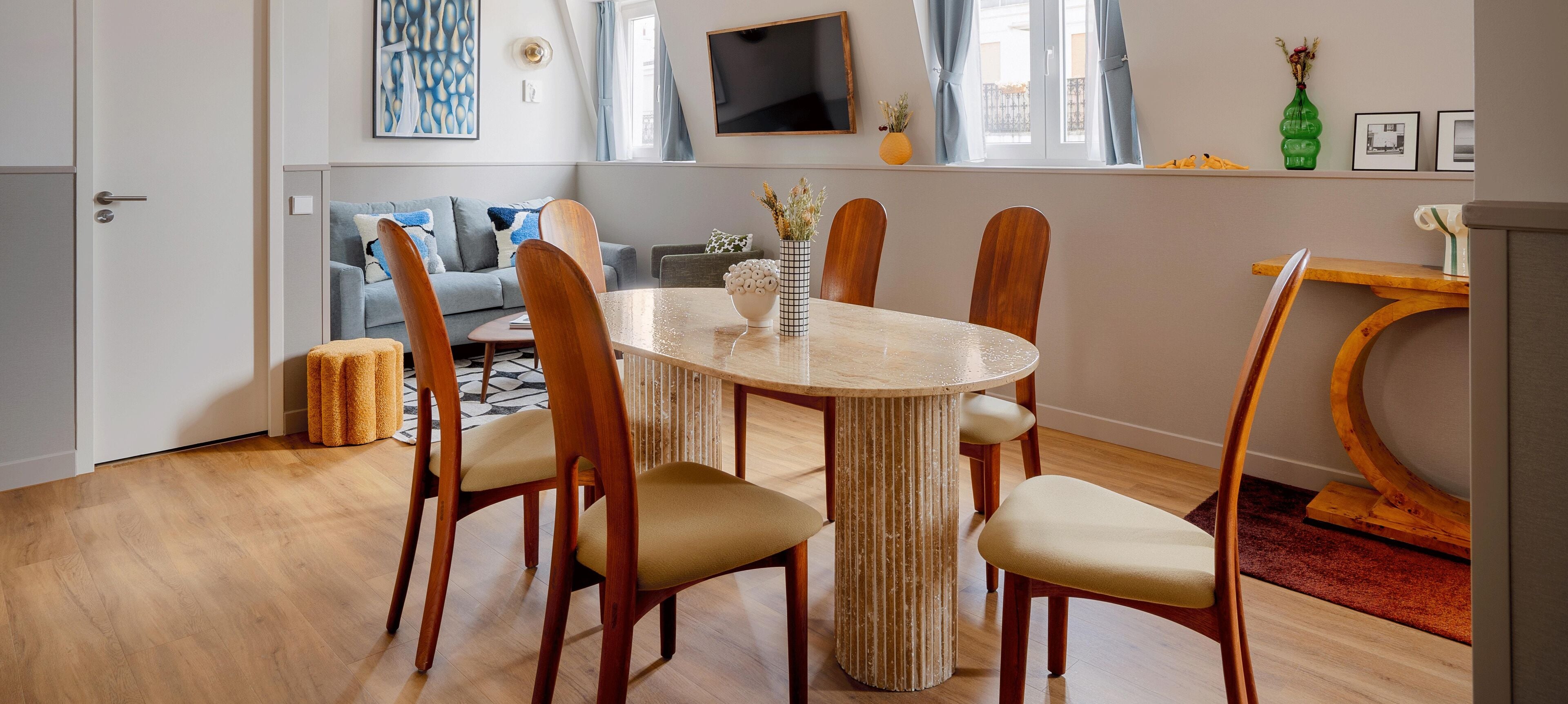 A dining area with a round table, six wooden chairs, and a vase with flowers.