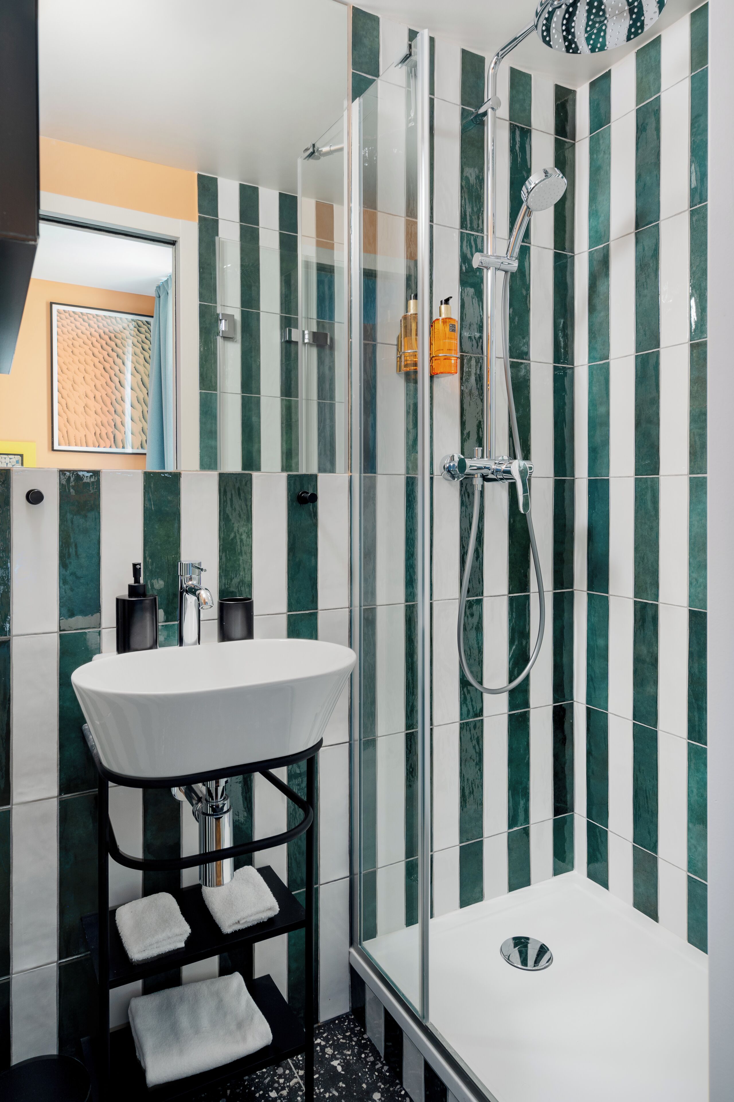 A modern bathroom with a glass-enclosed shower, a white sink, and striped green and white tiles.