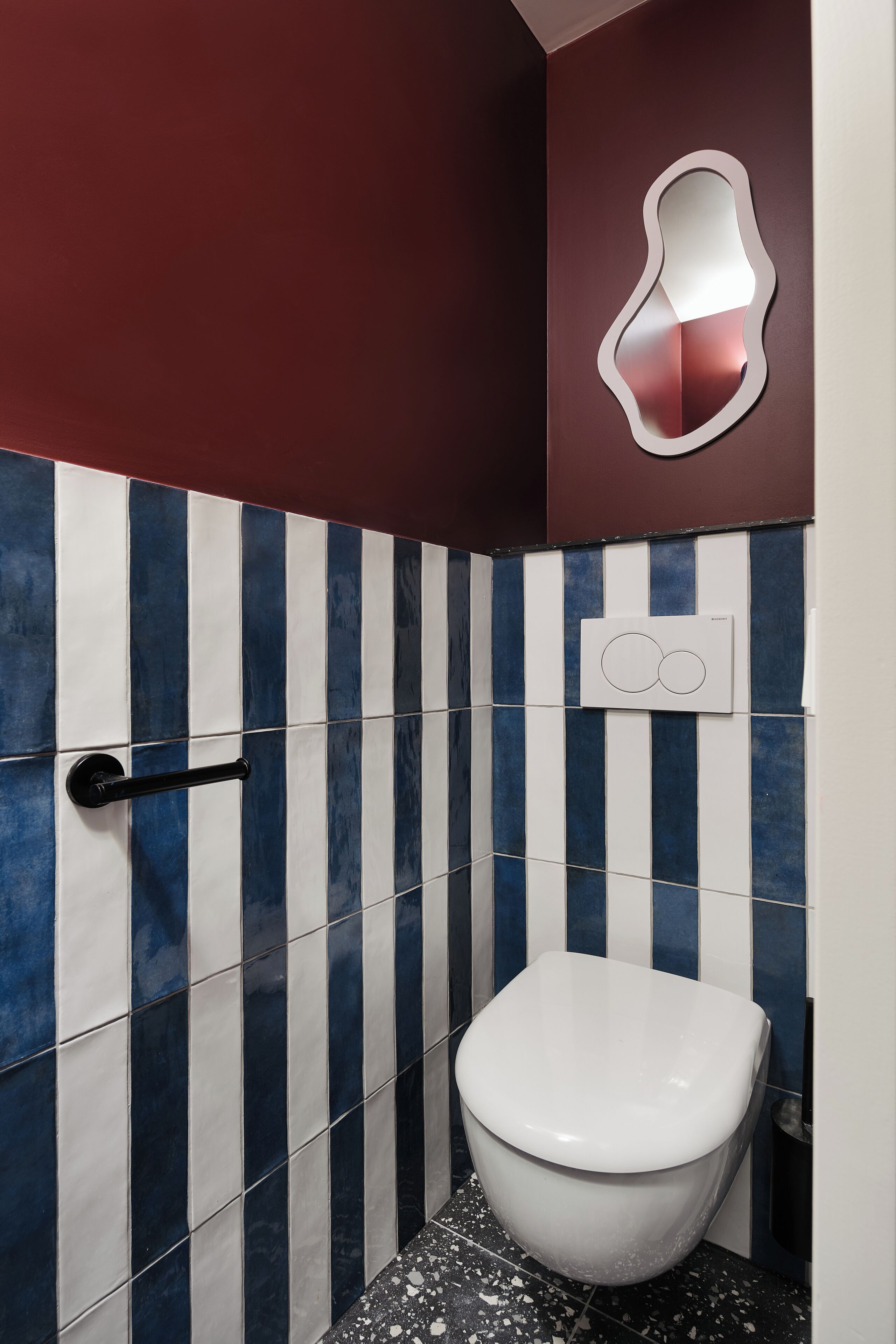 A bathroom with a striped tile wall, a white toilet, and a wall-mounted mirror.