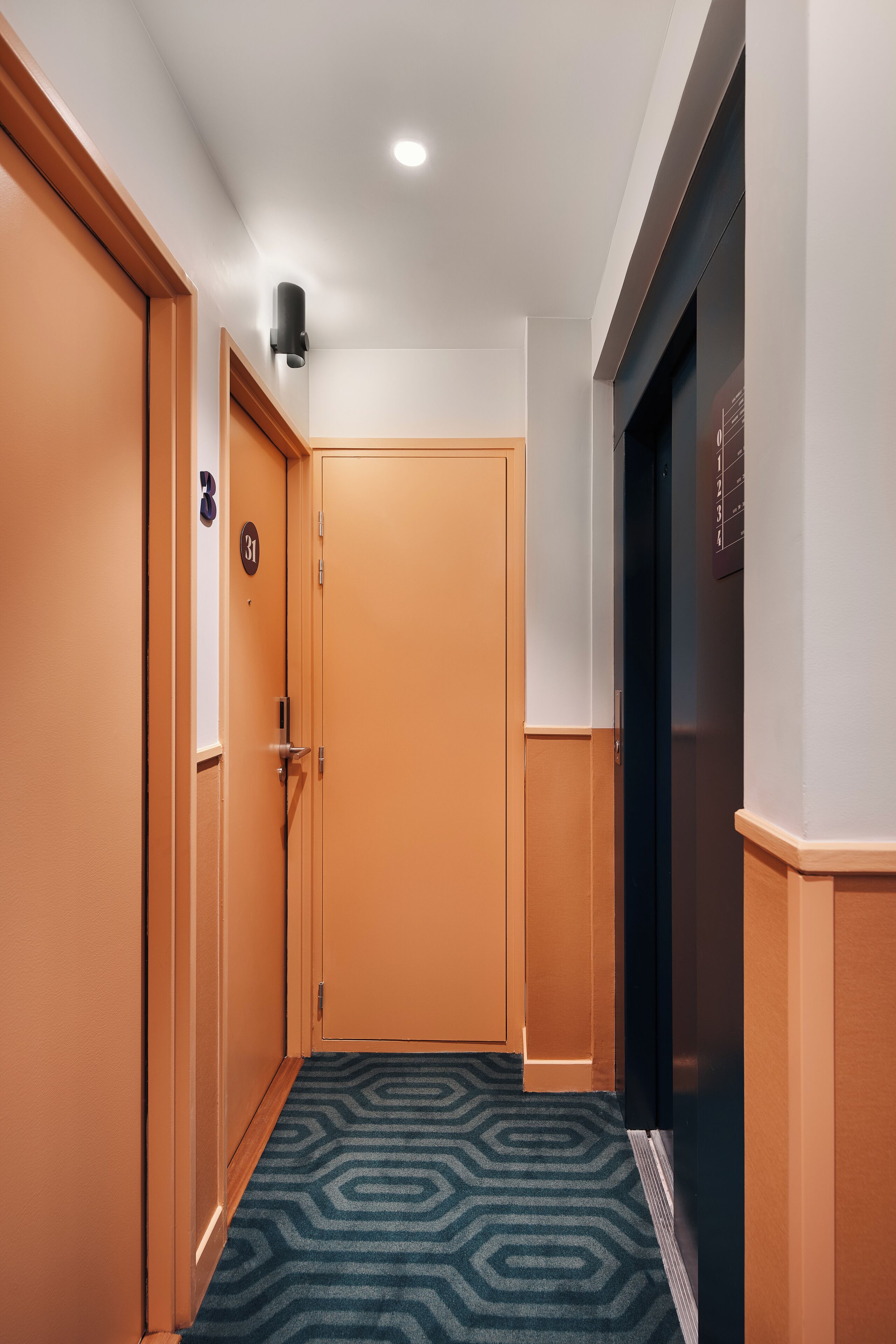 A hotel hallway with a carpeted floor, wooden doors, and a black elevator.