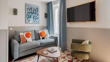 A modern living room with a grey sofa, a coffee table, a green armchair, a large abstract painting, and a flat-screen TV mounted on the wall.