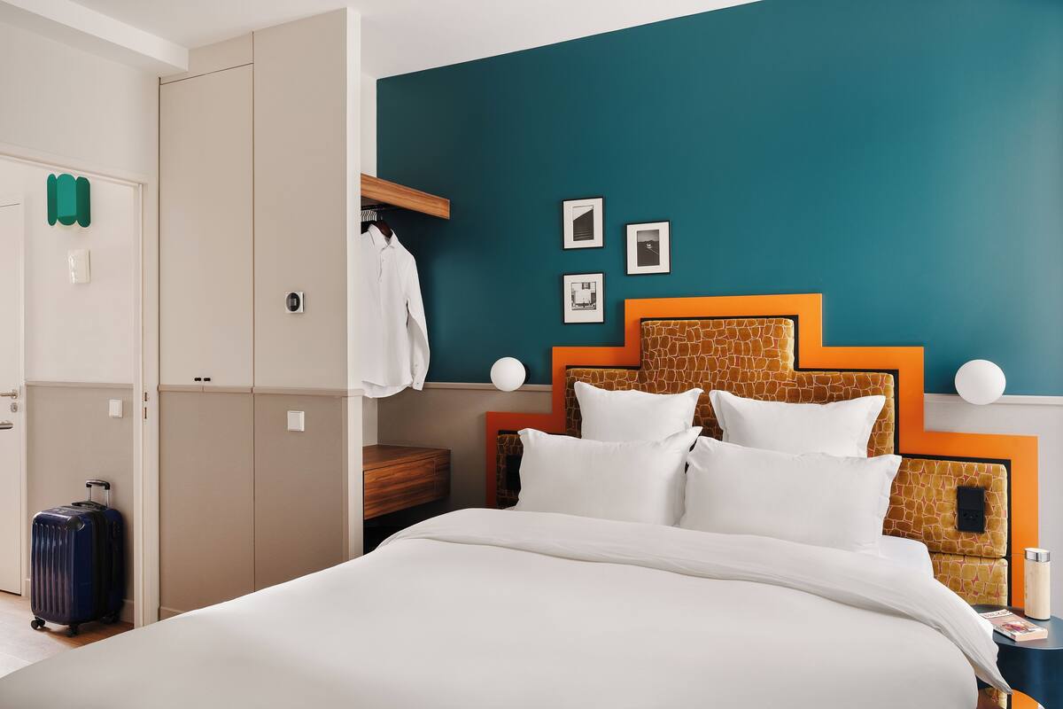 Een hotelkamer met een bed, een kledingkast, een koffer en een nachtkastje met een lamp.