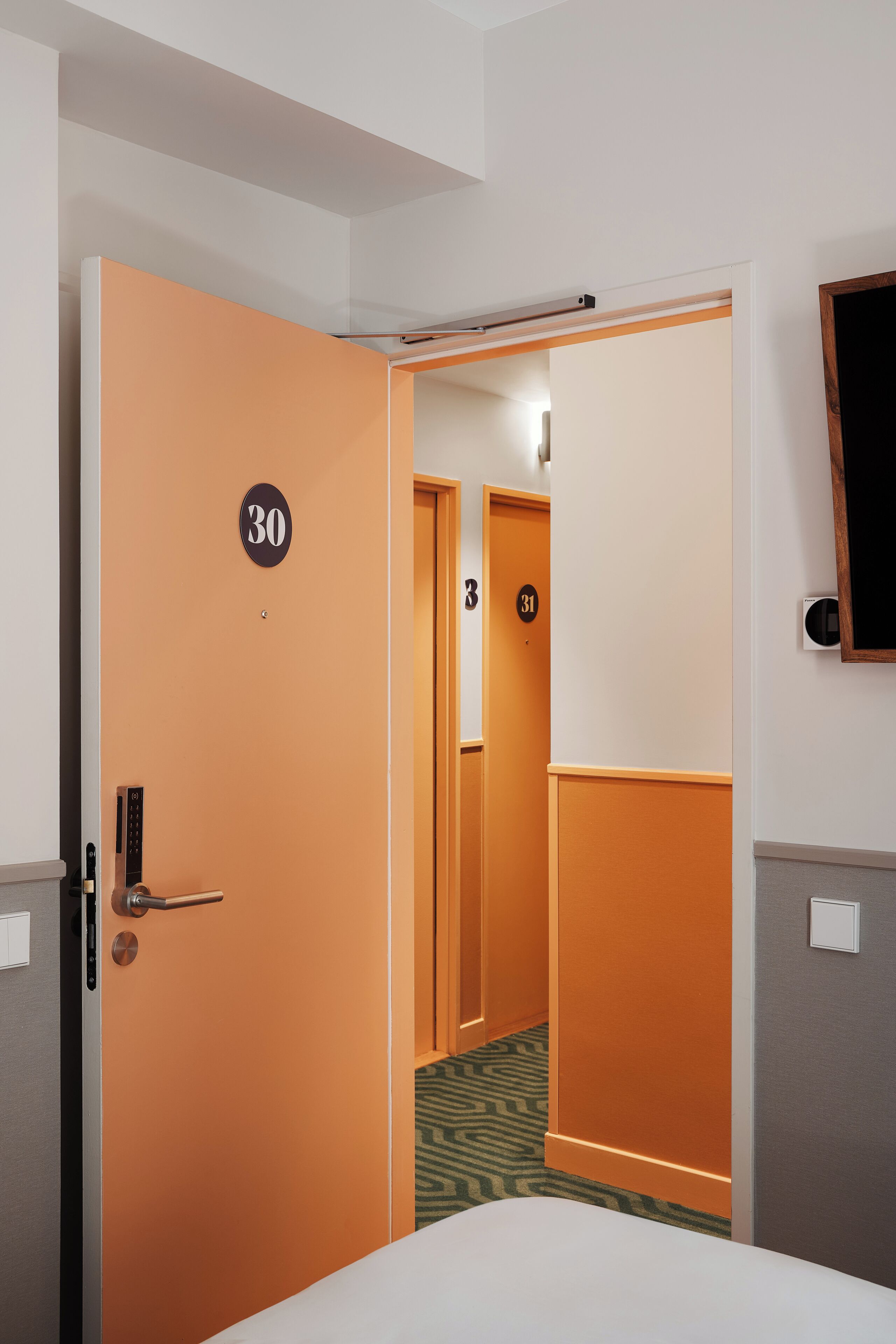 Une chambre d’hôtel avec un lit, une porte portant l’inscription « 30 », et un couloir menant à une autre chambre.