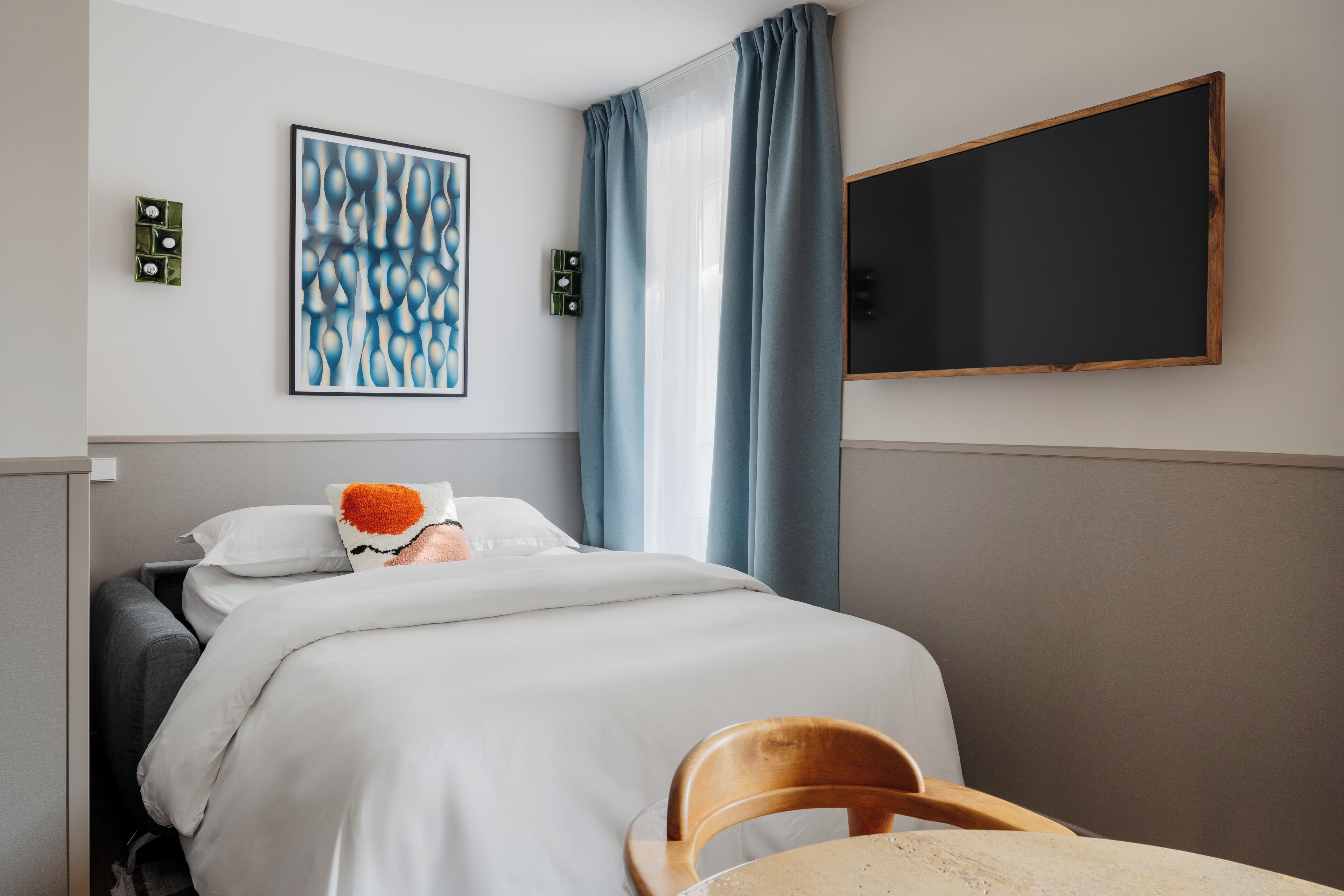 A hotel room with a bed, a chair, a painting, a blackboard, and curtains.