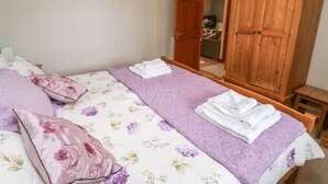 A bedroom with a bed, a wooden wardrobe, and a door leading to another room. - Otters Holt (South Molton)