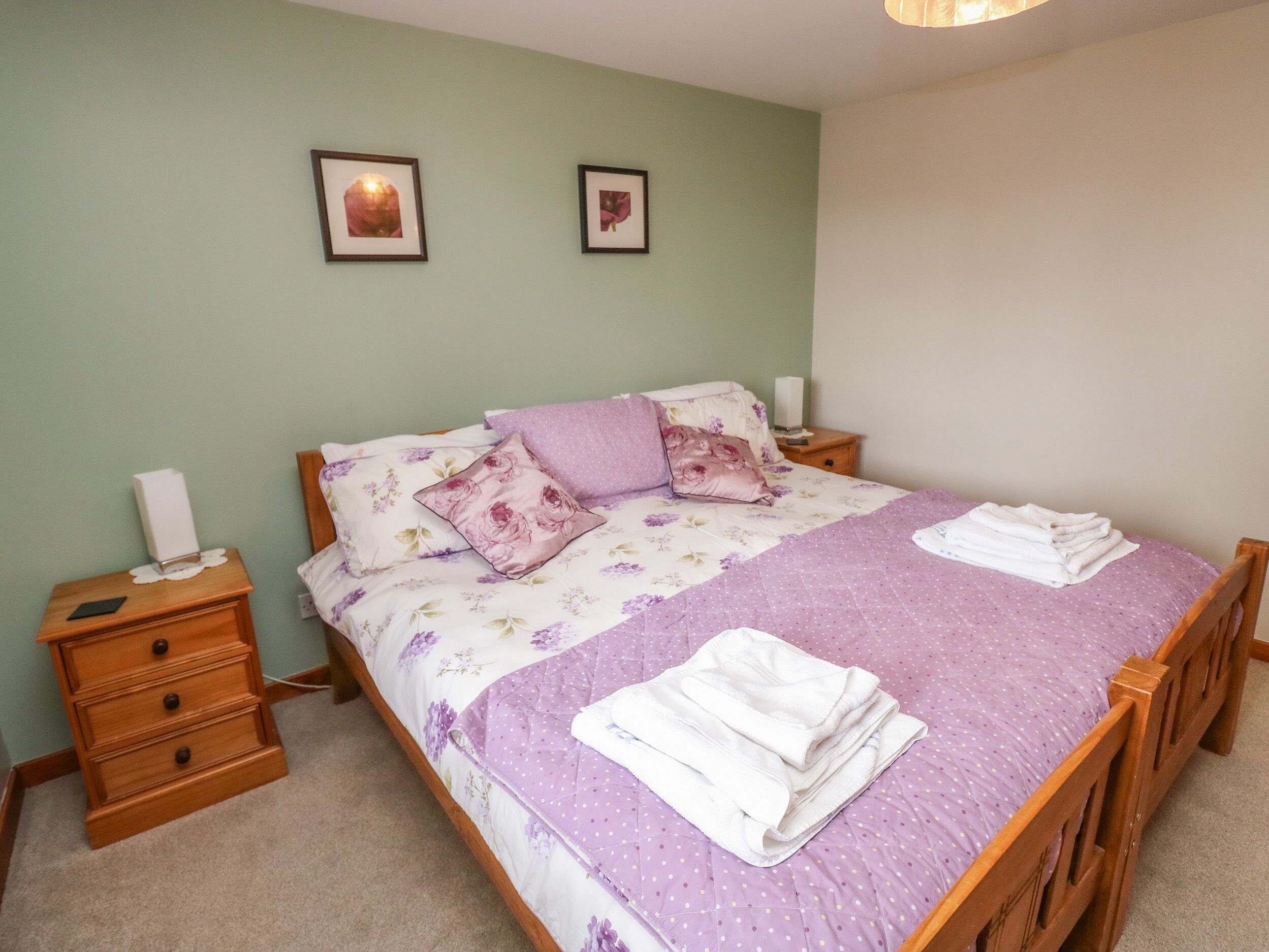 A neatly made bed with floral bedding and pillows, a bedside table with a lamp, and a framed picture on the wall.