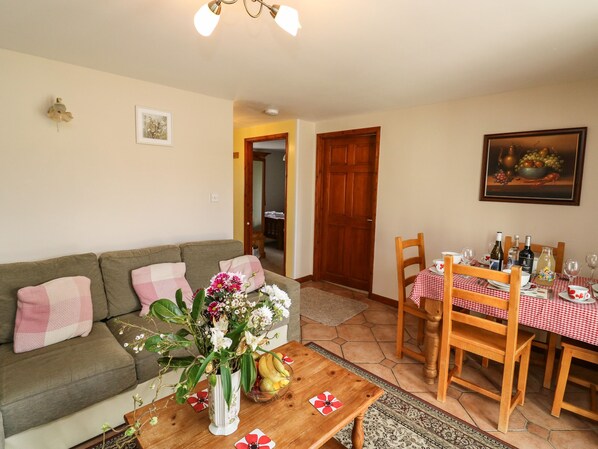 A cozy living room with a sofa, a coffee table with a vase of flowers, a dining table set with chairs, and a painting on the wall. - Otters Holt (South Molton)