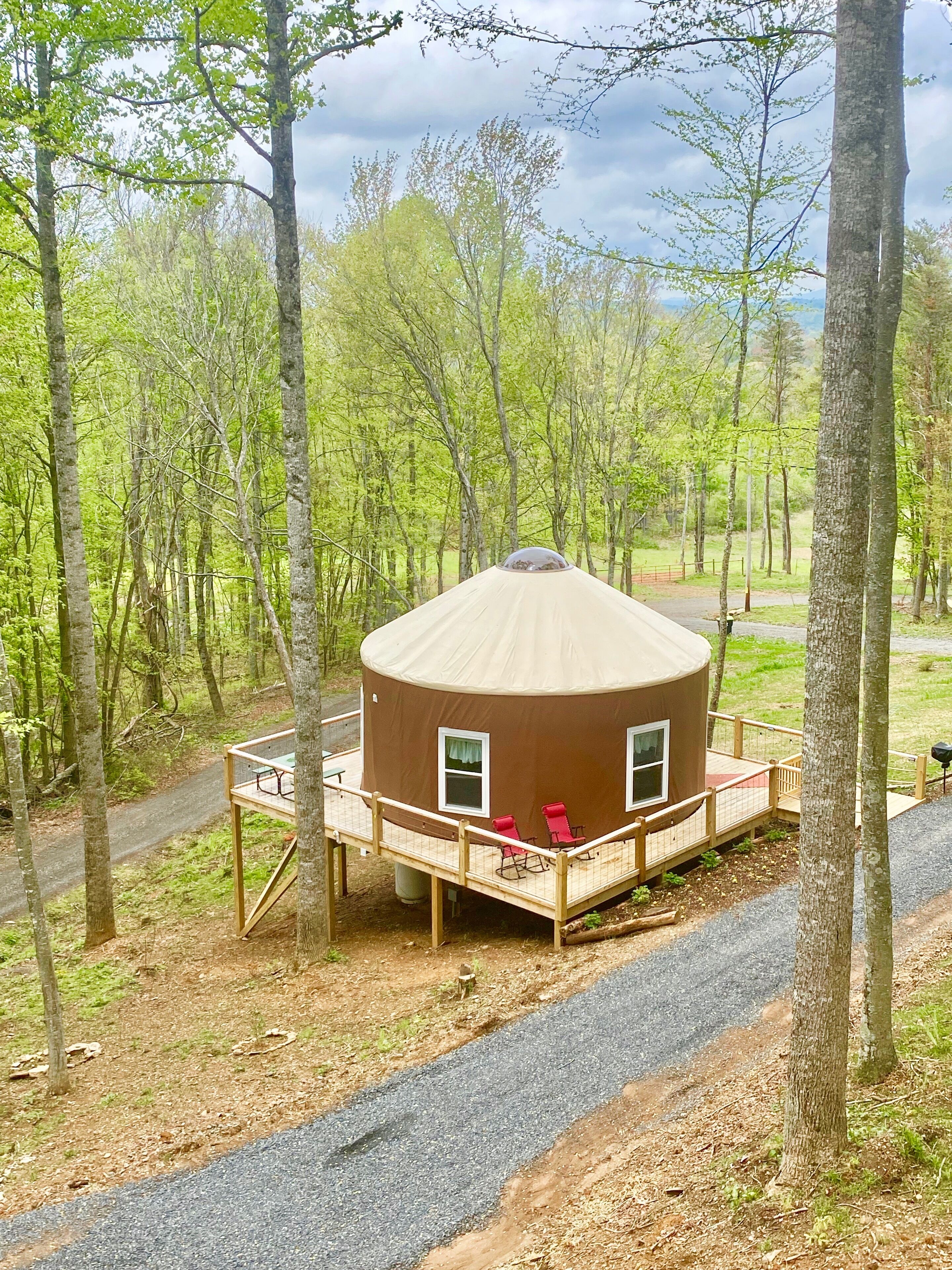 Une cabane ronde et brune, dotée d’une terrasse et de deux fenêtres, entourée d’arbres.